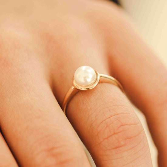 Auksinis žiedas su perlu dėvimas ant rankos
