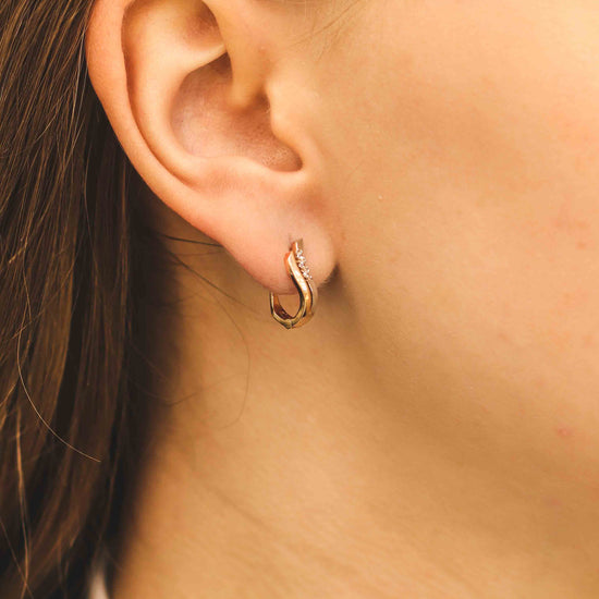 Eleganti viļņoti auskari rožu zeltā — modelim tuvplānā