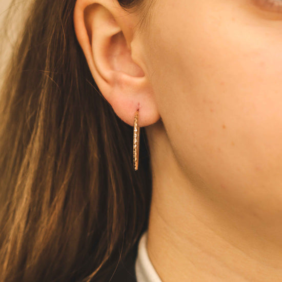 Plāns rozā zelta tekstūras stīpveida auskars uz modeļa