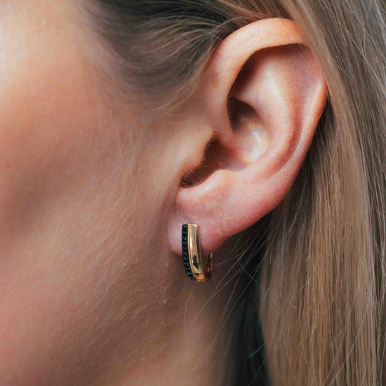 Rožinio aukso auskarai su juodais akmenimis ant modelio ausies