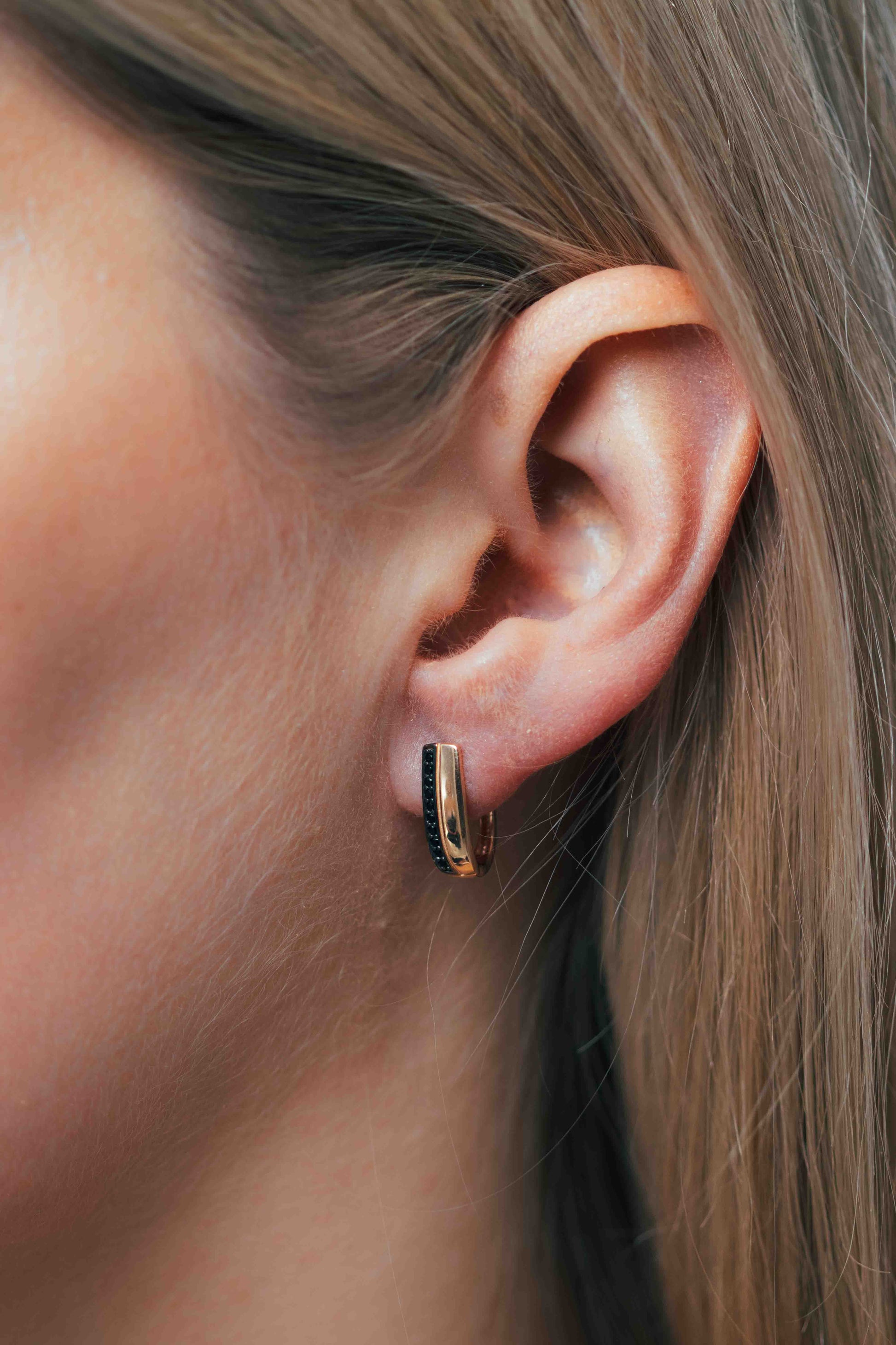 Rožinio aukso auskarai su juodais akmenimis ant modelio ausies