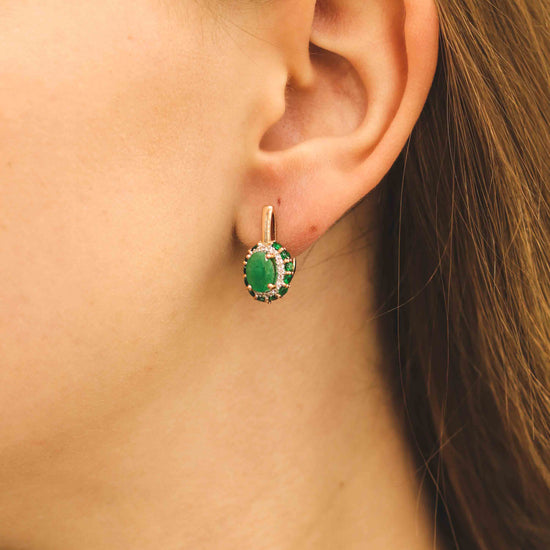 Moteris dėvi auskarus su ovaliu smaragdu