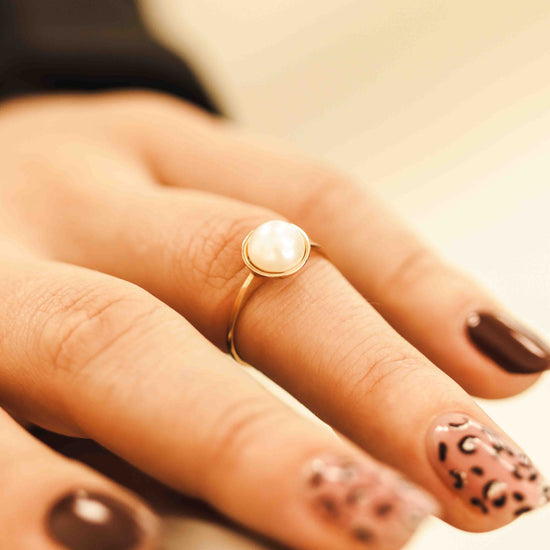 Rožinio aukso žiedas su perlu ant moters rankos