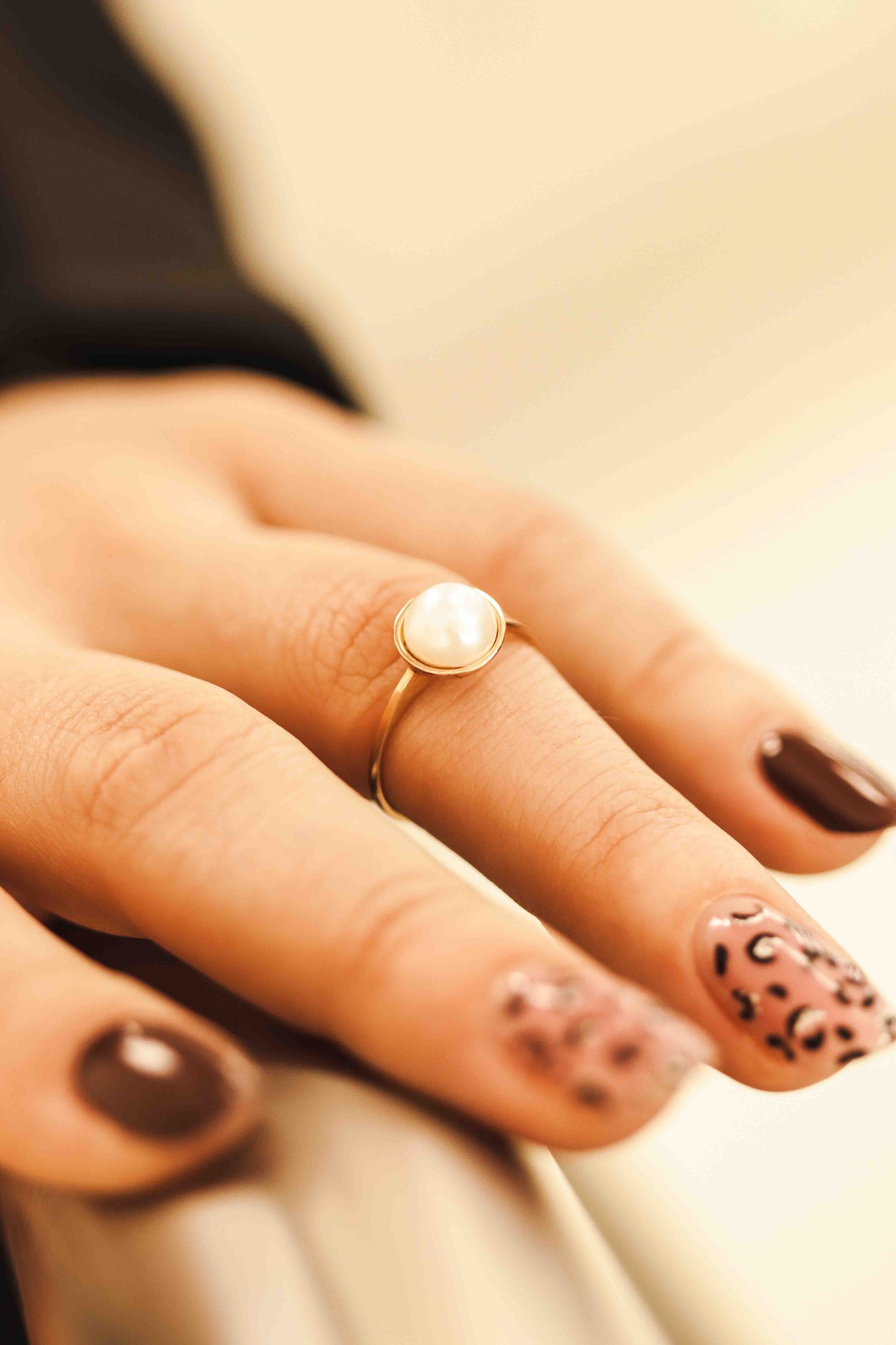 Rožinio aukso žiedas su perlu ant moters rankos